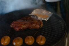 A steak and some tangerines are being grilled on a barbecue, with smoke rising around them.