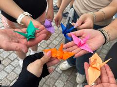 A group of people are holding colorful origami cranes in their hands, displaying the finished folded paper birds.