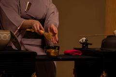 Daimyo Diary – Stroll with an Expert Guide at "Kenroku-tei" & Experience Traditional Tea Ceremony (With Breakfast) A person in a traditional kimono whisks matcha tea in a black bowl, surrounded by tea ceremony utensils.