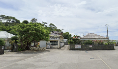 A street scene in Shioya Bay, Okinawa, with traditional Japanese buildings and lush greenery under a cloudy sky, evoking a sense of tranquility and cultural heritage.