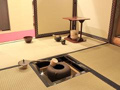 A traditional Japanese tea ceremony setting with tatami mats, a hearth, and tea utensils is depicted, evoking the concept of Wabi-sabi.