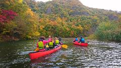 A group of people is canoeing on a river, surrounded by colorful autumn foliage.