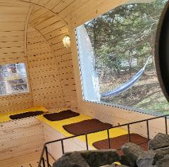 This is a sauna interior with wooden walls and benches covered in yellow towels and brown mats. A large window offers a view of a hammock outdoors.