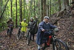 A large group of people with bicycles in a grassy area with trees and mountains in the background.