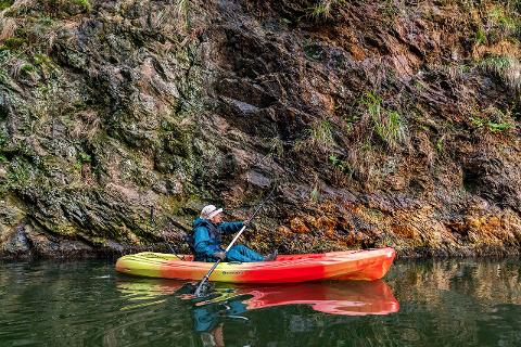 Fukui Morning Kayak Tour – Explore the Five Lakes of Japan A person kayaks by a rocky cliff face with moss and vegetation, reflecting in the water.