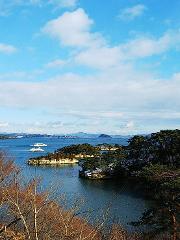 A picturesque view of blue waters dotted with small islands covered in evergreen trees, under a partly cloudy sky, with two boats sailing on the water.