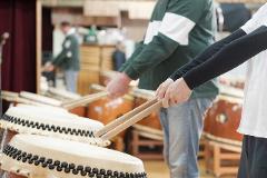 Two people are playing the taiko drums with sticks.