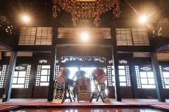 Two taiko drums are set up inside a traditional Japanese building with sunlight streaming through the windows and a chandelier overhead.