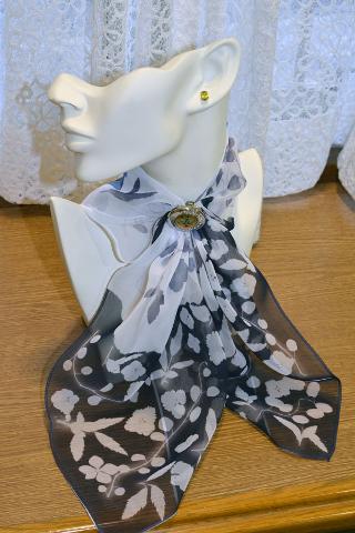 A mannequin head displays a black and white floral scarf secured with a vintage brooch and accessorized with an earring.