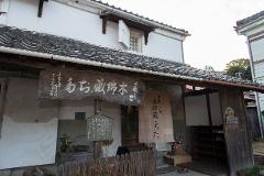 A traditional Japanese building with dark tiled roofs, wooden signs, and a display of shoes greets visitors at the Chita Cotton Museum.