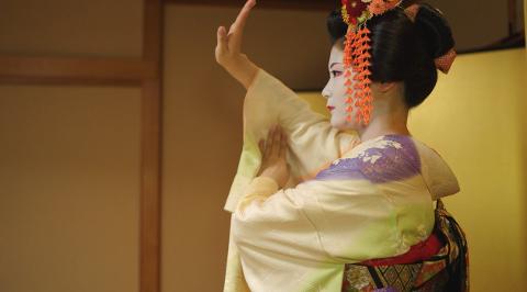 A geisha in traditional attire performs a graceful dance in a Japanese restaurant.