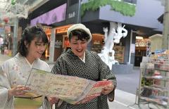 Two women in kimonos happily look at a map together in a colorful arcade.