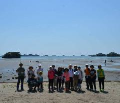 A group of people pose for a picture on a beach with a calm ocean and several small islands in the background.