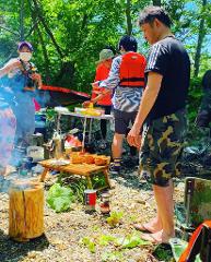 Des gens se sont rassemblés près de la rivière Shiodomari lors de l&#39;excursion d&#39;une demi-journée en canoë, avec une table, du matériel de cuisine et un support de feu de bois au premier plan.