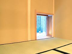 A traditional Japanese room with tatami mats looks out onto a serene bamboo garden through an open doorway.