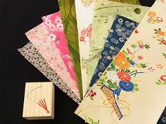 A fan motif is carved into a small wooden box next to a collection of colorful, patterned papers.