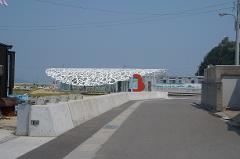 A ground-level shot of a gray asphalt road leading towards a building with an intricate white roof and a red sign on the side.