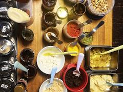 A top-down shot of a table filled with a variety of ingredients, including spices, sauces, fruits, and marshmallows, each with its own spoon or utensil.