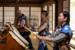 A group of people in traditional Japanese clothing play taiko drums during a performance.