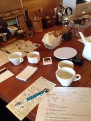A coffee tasting session is set up on a wooden table with coffee brewing equipment, cups, and instruction sheets.