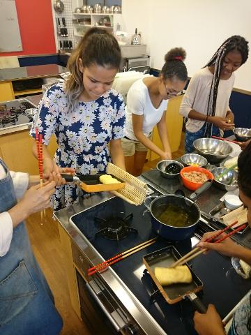 A group of people are in a kitchen preparing food, using chopsticks to cook omelettes and organize ingredients into bowls.