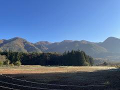 Explore the Local Morning Charm of Shiobara Onsen with a Satoyama Mini-Trek and Local Breakfast Delight A crisp morning mist settles over a rural landscape in Shiobara Onsen, with a field in the foreground and rolling, autumn-colored mountains under a clear blue sky.