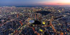 Sunset Departure! Tokyo Helicopter Cruise for 5 – Experience Dusk and Nighttime Cityscapes (Tokyo) An aerial view of Tokyo at dusk showcases a sprawling cityscape illuminated by countless lights, with a prominent dome stadium visible among the towering buildings.