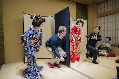 Geisha Ozashiki at Asakusa, a Quality Time Filled with Art and Japanese Culture A man in casual clothes crouches as two geishas and two women in traditional attire observe in a room with shoji screens.
