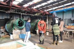 A group of people stand in front of a large industrial machine, possibly on a tour of an agar factory.