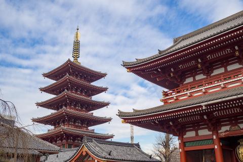 A five-story pagoda and traditional red buildings stand against a cloudy blue sky.