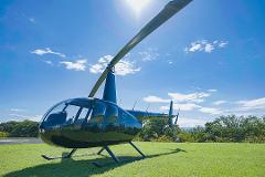Private Helicopter Tour of Tokyo A black Robinson R44 helicopter sits on a grassy helipad under a bright blue sky with scattered clouds, ready for a private tour.