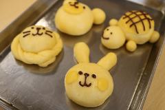 A variety of animal-shaped bread buns, including a rabbit, bear, turtle, and cat, are arranged on a silver baking sheet.