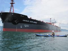 A kayaker paddles near the massive cargo ship "UNIQUE EXPLORER" on the water.