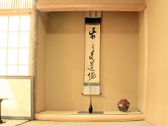 A serene Japanese alcove displays a calligraphy scroll, a minimalist vase with a single sprig, and a rustic ceramic jar, embodying the essence of Wabi-sabi.