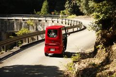 A bright red EV-TUKTUK drives on a winding road in a lush green forest.