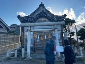 Two people stand before a traditional Japanese shrine with a torii gate in front, as seen on the Shika Town Walking Tour page.