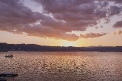 A serene sunset paints the sky with warm hues over a tranquil lake, with silhouetted mountains and a small island dotting the landscape.