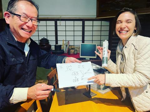 A man and a woman are smiling and presenting a whiteboard with Japanese tea terminology and a package of tea in a shop in Hakodate.