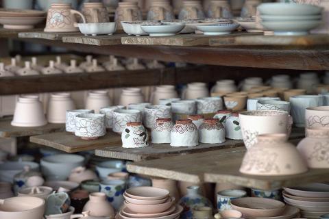 Ceramică și porțelan: Povești ale artizanilor din spatele meșteșugului A group of people on a tour look at artisans working in a pottery studio.