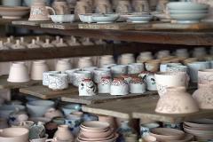 Ceramică și porțelan: Povești ale artizanilor din spatele meșteșugului A group of people on a tour look at artisans working in a pottery studio.