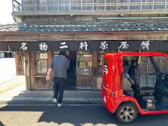 A person walks towards a traditional Japanese building with a red electric vehicle parked in front.