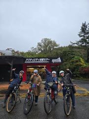 Two e-bikes are parked in a grassy field of yellow flowers with houses and green hills in the background.