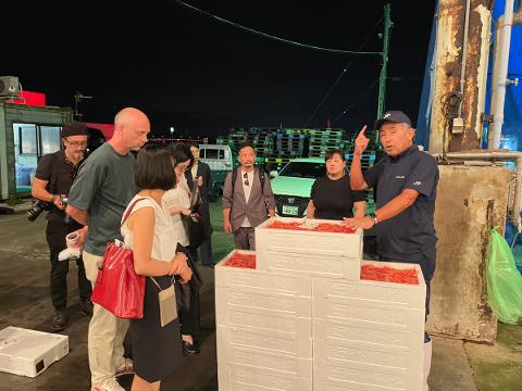A group of people, including a tour guide, observe a display of seafood at the Kanazawa Wholesale Market.