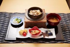 "Reborn-Art" Tour: Experience Contemporary Art on the Oshika Peninsula A Japanese meal featuring rice with mushrooms and chicken, soup, tamagoyaki, pickled vegetables, and a dish of eggplant is presented on a dark tray with a patterned runner.