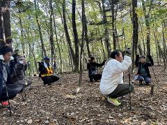 Explore the Local Morning Charm of Shiobara Onsen with a Satoyama Mini-Trek and Local Breakfast Delight A group of hikers with trekking poles crouch on a forest floor covered in fallen leaves.