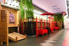 A Japanese-themed decor in a hallway featuring a bamboo ladder, red benches, lanterns, and decorative trees.