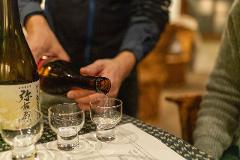 A server pours sake from a bottle into small glasses at a tasting session in a historic brewery.