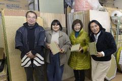 Four people stand in a room with tatami mats, holding small samples of tatami.
