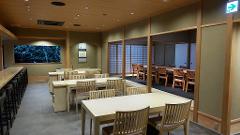 Daimyo Diary – Stroll with an Expert Guide at "Kenroku-tei" & Experience Japanese Martial Art "Kyudo" (With Breakfast) A well-lit, traditional Japanese dining room with multiple tables and chairs, featuring a bar on the left and sliding doors on the right.