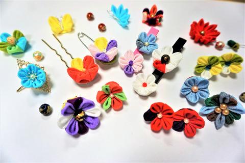 A collection of colorful fabric flowers, some attached to hairpins and a barrette, are displayed on a white background.